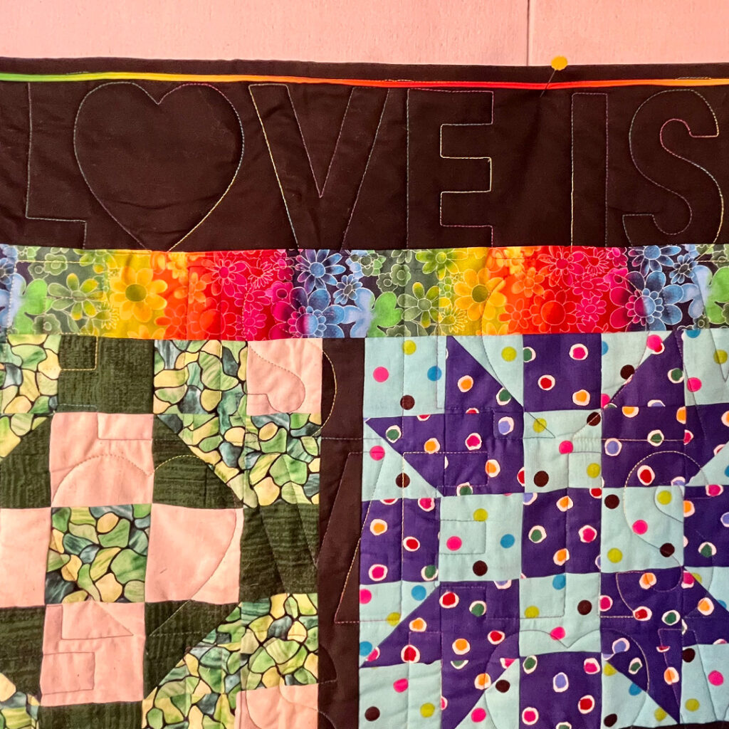 Quilted design around the perimeter of the quilt partially visible shows the words Love is Love.