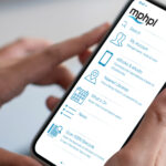 A person holding a cell phone and MPHPL Mobile App interface text on cell phone screen, ‘MPHPL My Account, eBooks & eAudio, Nearest Libraries, What’s On, News, Scan ISBN Barcode.’