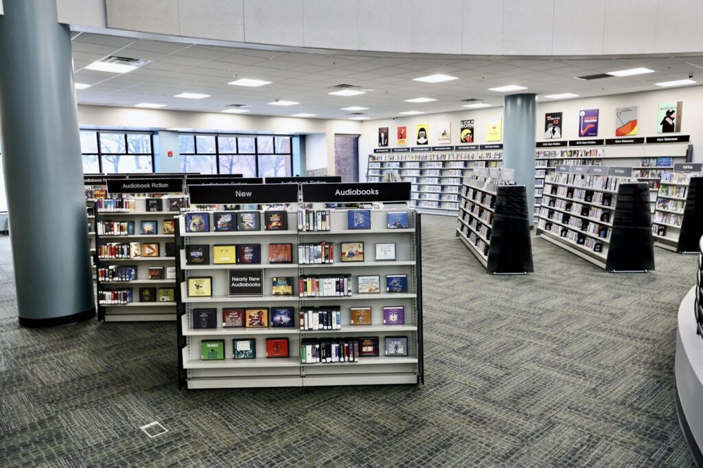 Displays containing media content available for cardholders to check out. Image text visible on displays, ‘New, Audiobooks, Audiobook Fiction.’