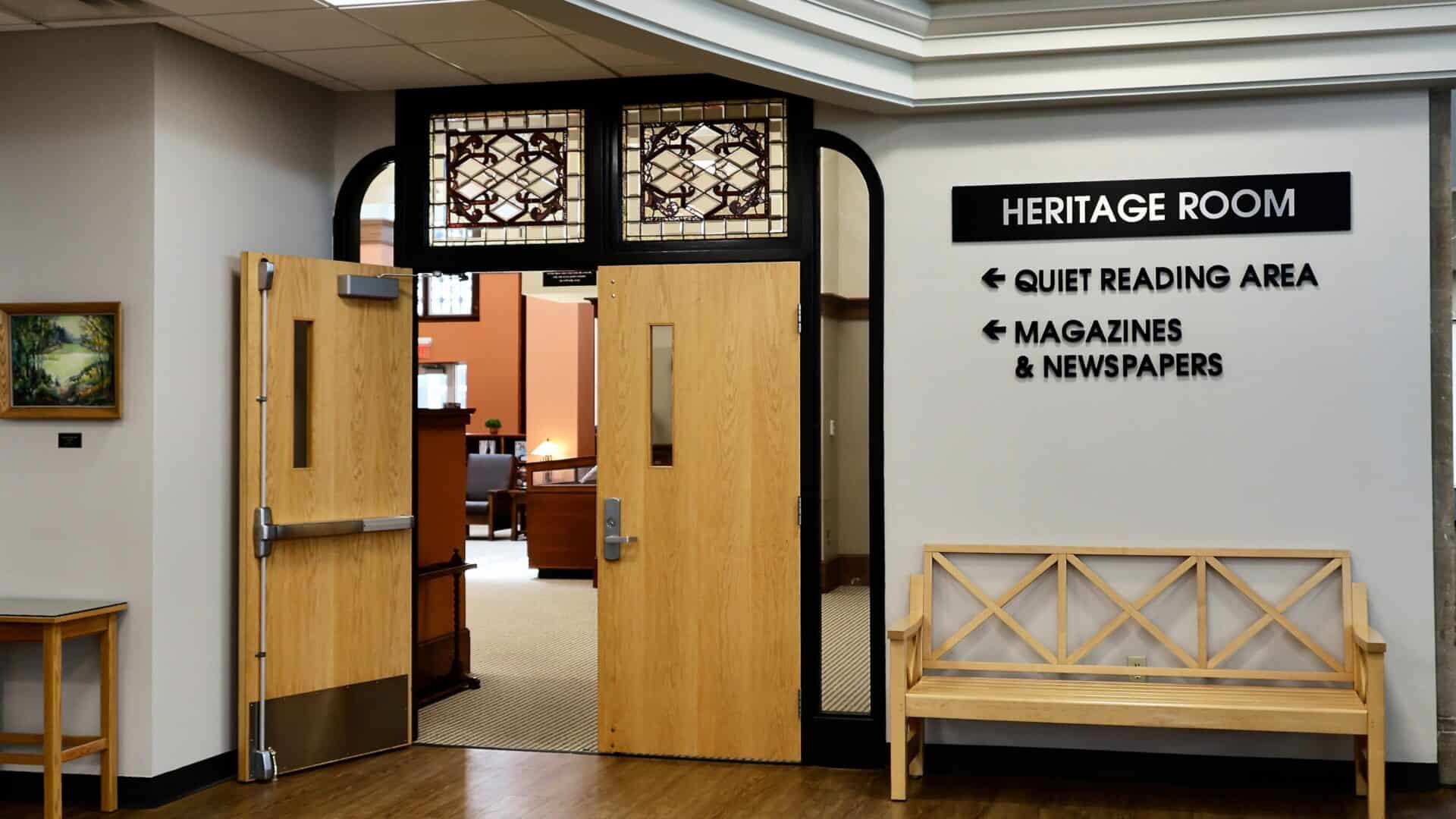 The entrance of the Mishawaka Library Heritage room with two stained glass windows above two large wooden doors.
