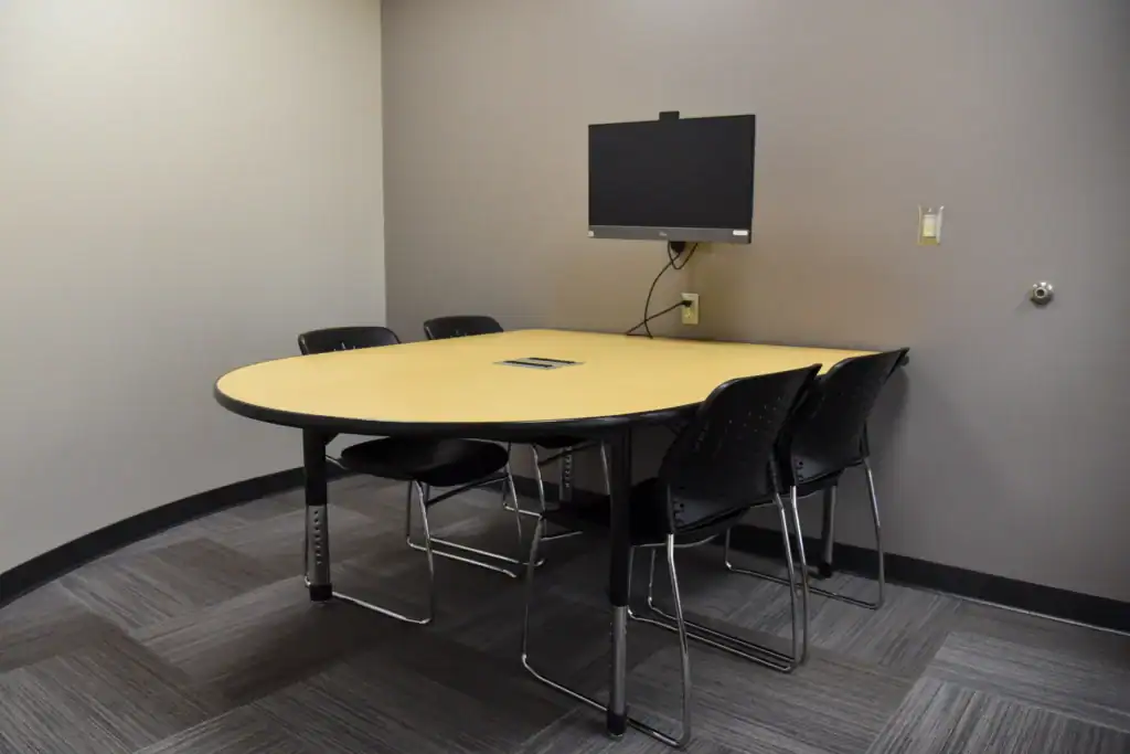The Mishawaka Library Adult Study Room One containing a table against the back wall, four chairs and a monitor mounted on the wall above the table.