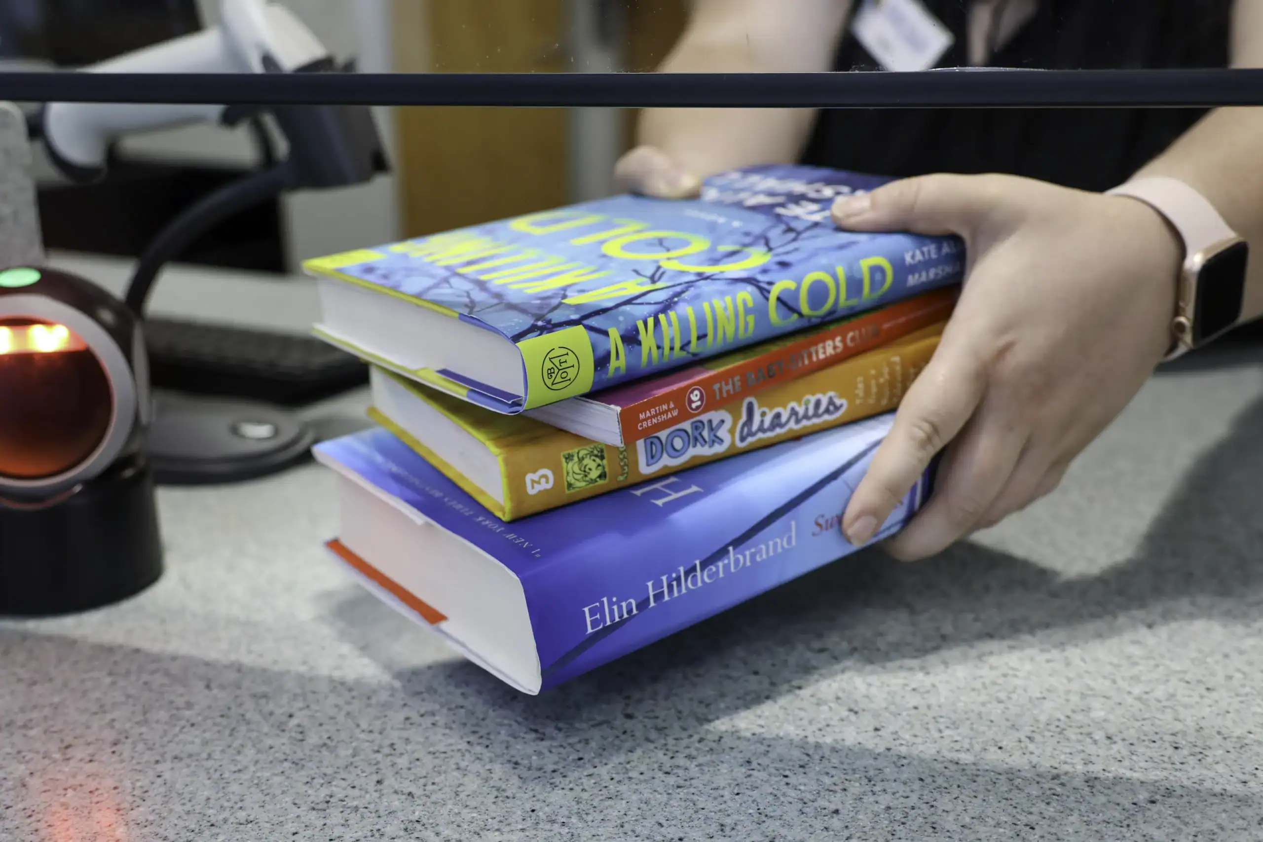 An MPHPL staff member picks up a stack of four chapter books at the checkout desk.