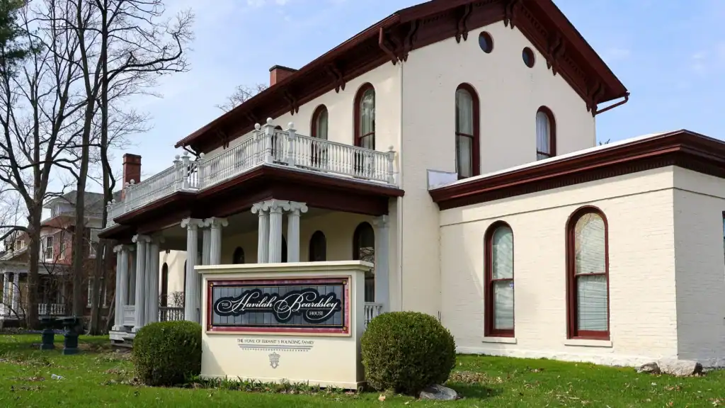 A large cream-colored brick house with arched windows, a wraparound porch, and a red-brown roof. A sign in front reads “Harold L. Bradley” and “The School of Graduate Studies & Research.”.