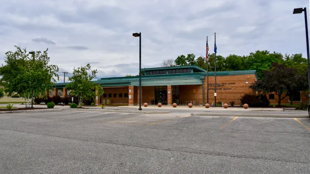 Exterior of the Mishawaka-Penn-Harris Public Library Bitter-Sweet Branch, a single-story brick building with a teal roof and a parking lot in the foreground.