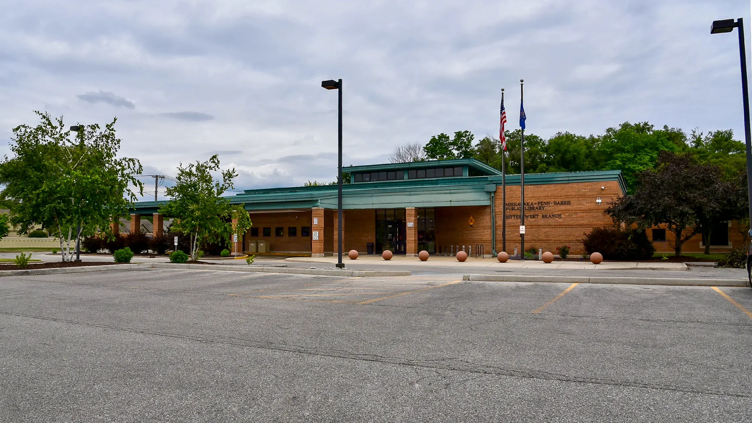 Exterior of the Mishawaka-Penn-Harris Public Library Bitter-Sweet Branch, a single-story brick building with a teal roof and a parking lot in the foreground.